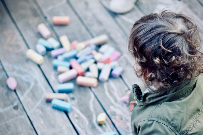 Child drawing with chalk on a wooden deck floor.