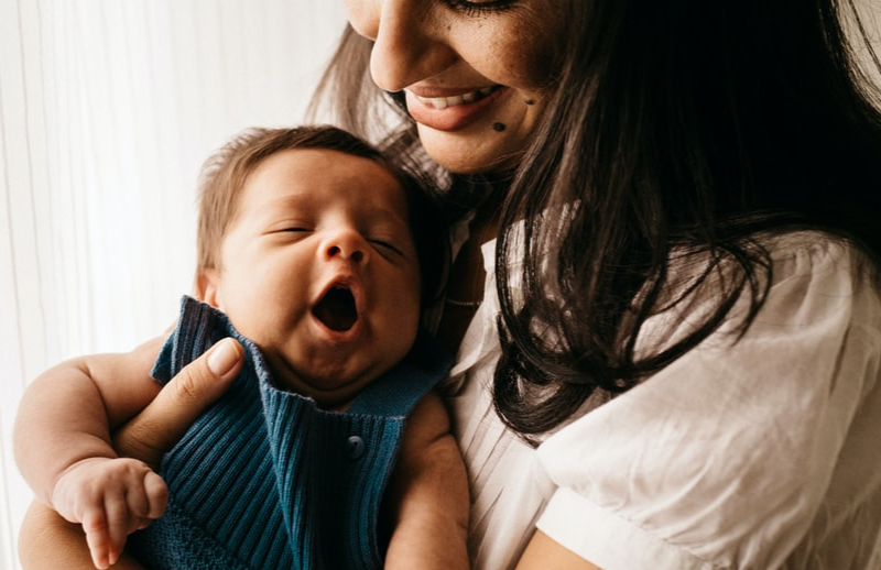 Woman holding a yawning baby in her arms.