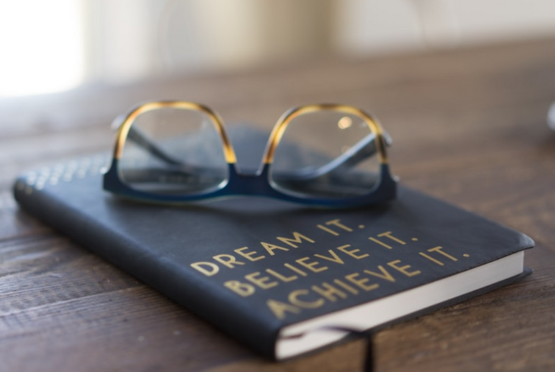 A book on a table. The book is inscribed with the words 'Dream it. Believe it. Achieve it.'