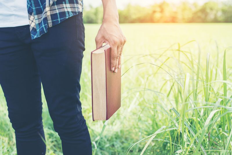 A person bolding a religious book in a field.