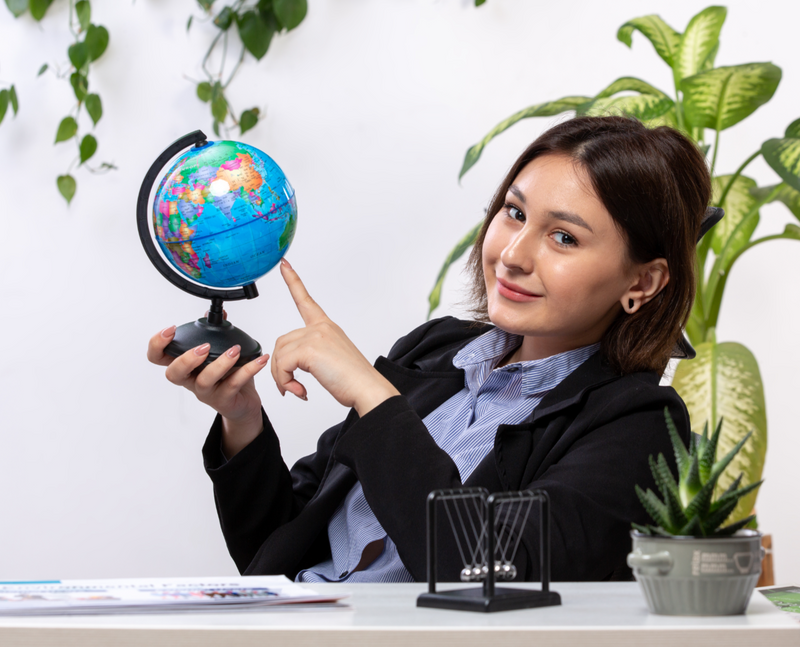 A young business woman holds a globe and smiles.