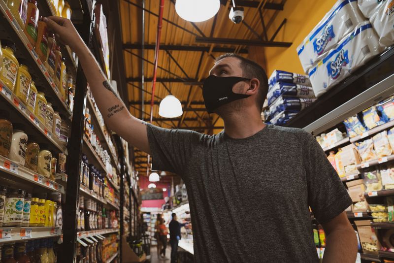 A man wearing a mask chooses an item from a grocery shelf.