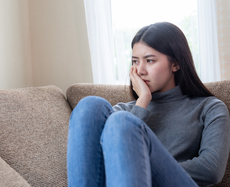 young woman sitting sadly on the couch looking worried