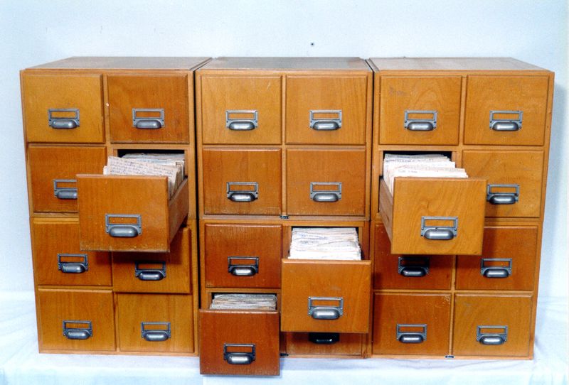 A wooden Zettelkasten with six columns comprising of four drawers each.  Some drawers are open, filled with notes to the brim