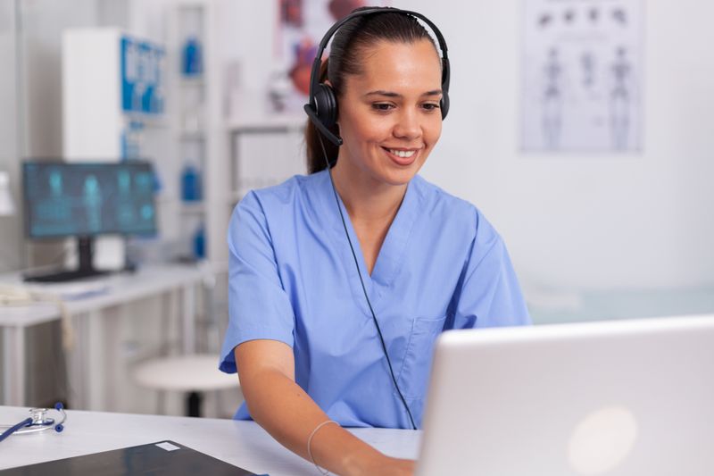 A photograph of a female medical secretary wearing a headset working on an office computer.