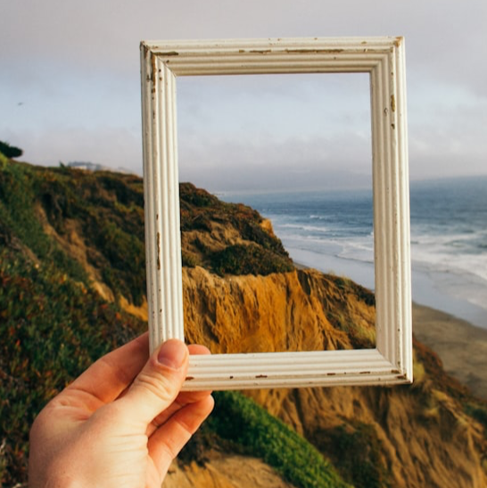 A hand holding an empty picture frame against a landscape.