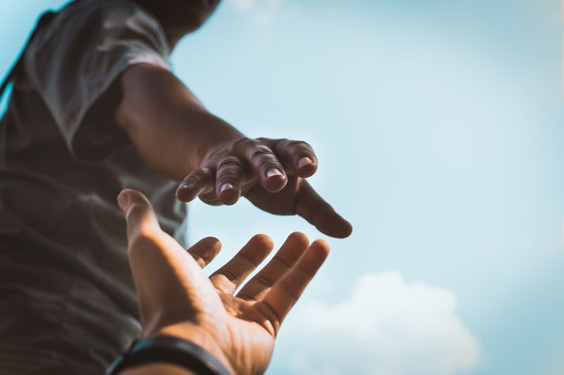 Someone's hand reaching down to catch another person's hand.