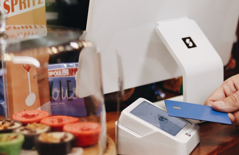 A person tapping a bank card on a point of sale payment system.