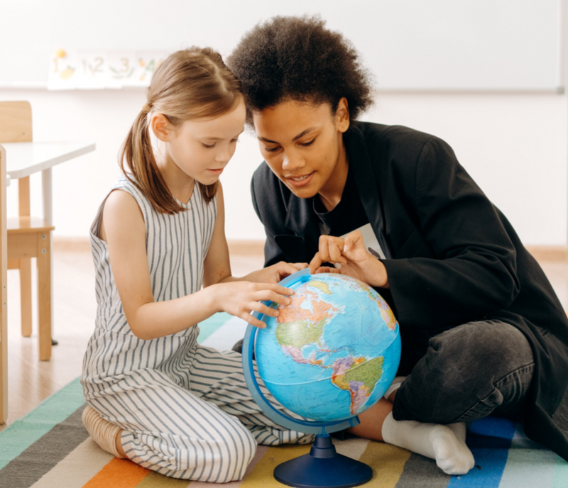 A female teacher and female elementary school student looking at a globe of the earth.