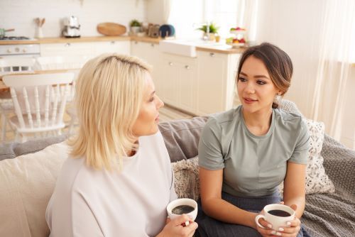 two female friends-are-sitting-chatting-couch drinking coffee