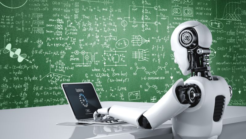 A robot sitting at a desk in front of a green chalkboard filled with mathematical equations. 