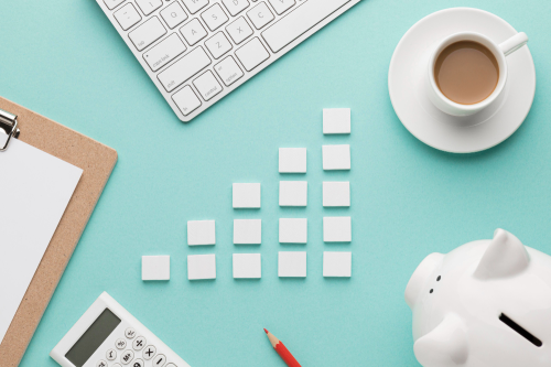 Desk with coffee, piggy bank, calculator, clipboard. Small cards arranged as a habit stack to show financial growth.