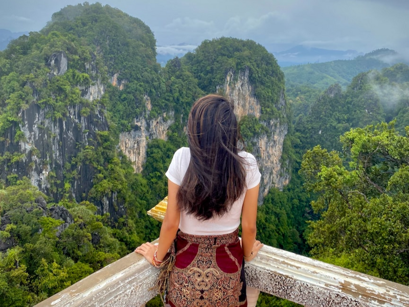 Person, standing at the edge of a balcony, looking out at the mountains.