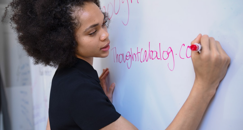 A Black woman writing on a whiteboard at work.