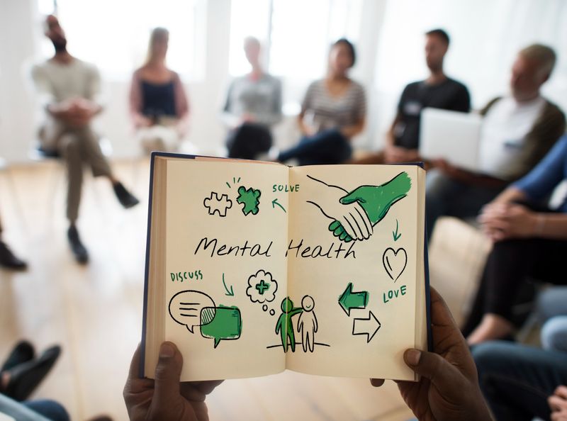 Group therapy session with someone holding a sketchbook with images representing mental health symbols 