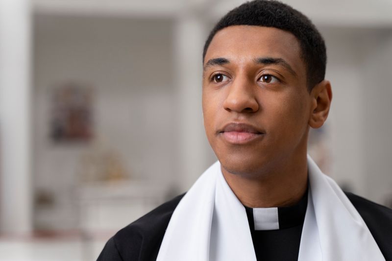 A young African-American priest wearing a robe and collar.