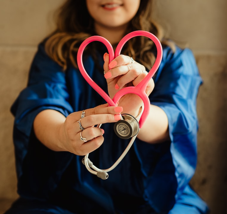 Woman holding a red stethoscope in the shape of a heart.