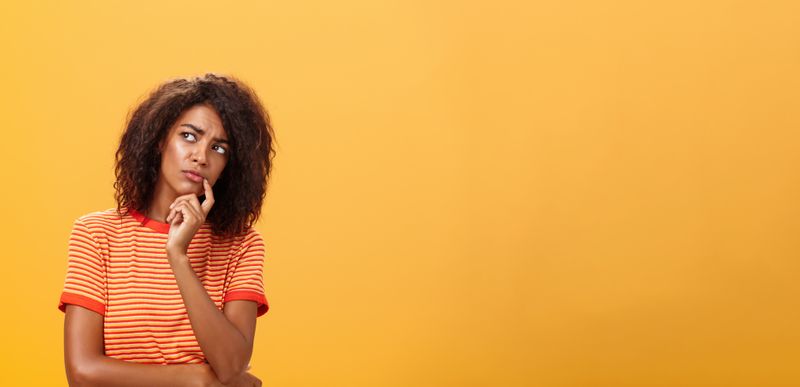 A woman with her hand on her chin with a thinking face as she looks up.