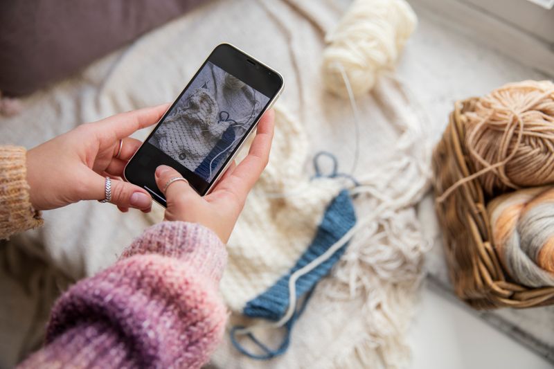 Hands holding a smartphone while taking a photo of a crochet project.