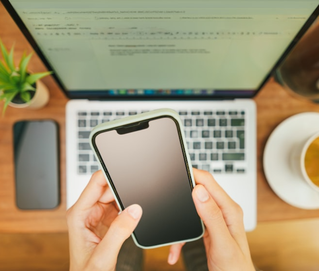 A person holding up a phone in front of a laptop.