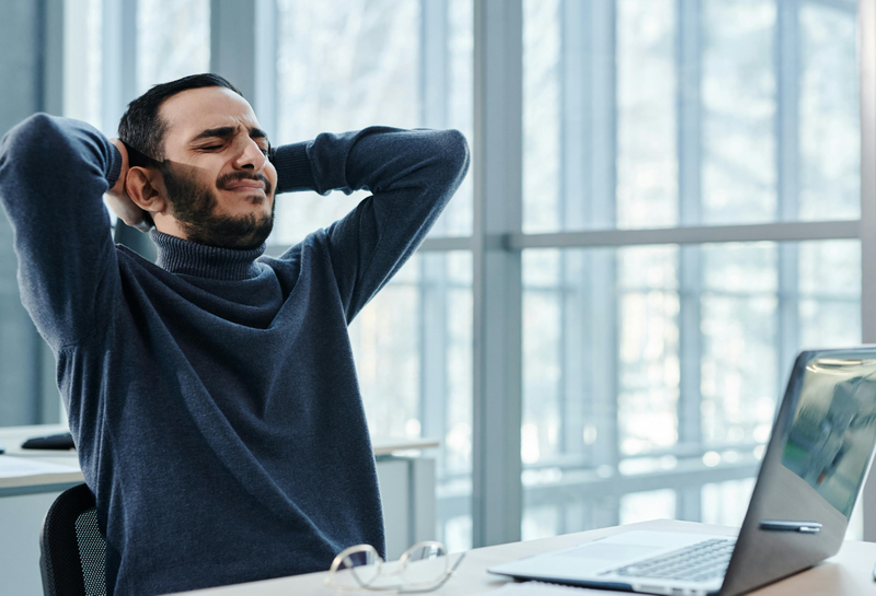 Man leaning back in office chair, appearing stressed amidst a busy workday, reflecting.