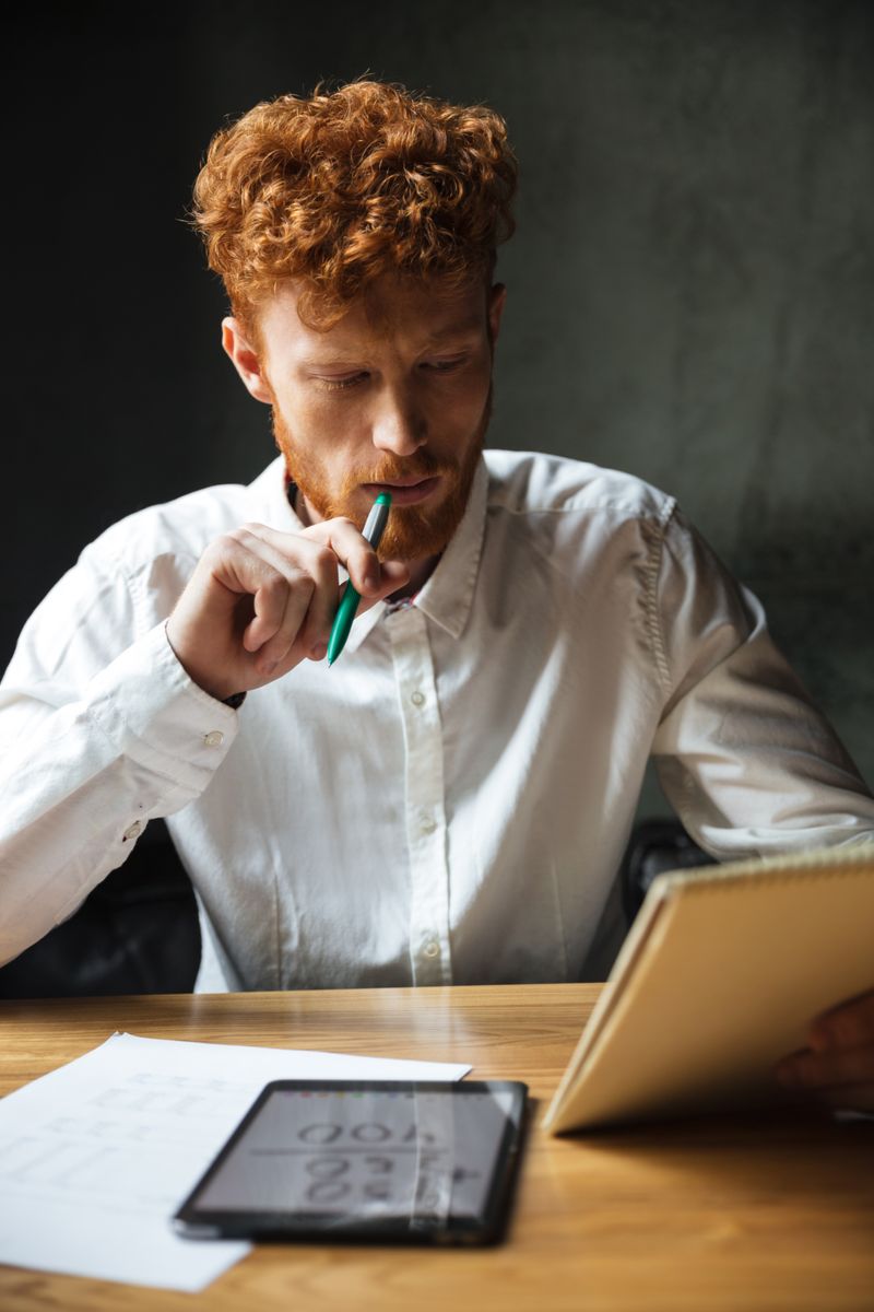 Young man in a white shirt thinking as he works on the computer.