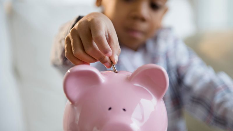 A kid putting money into a piggy bank