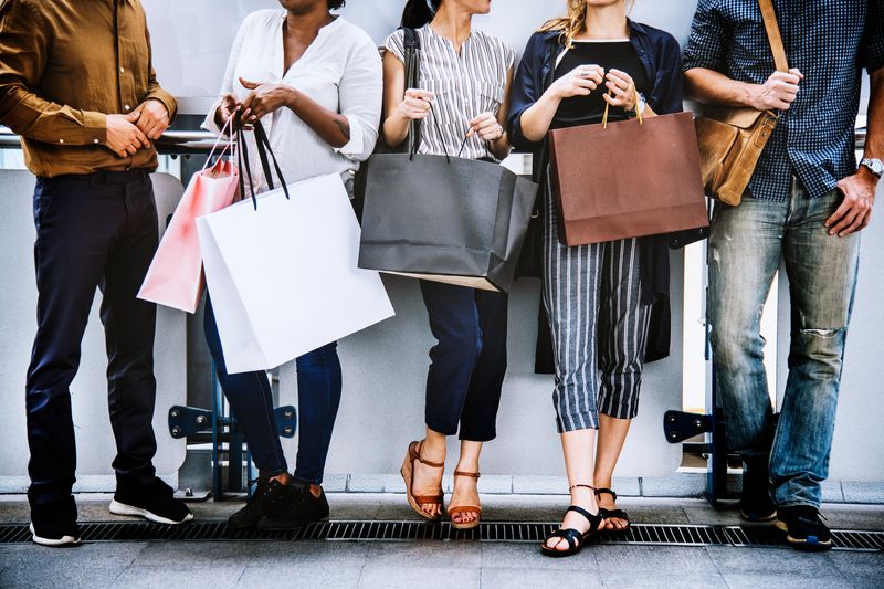 five people of different ethnicities and genders carrying shopping bags, in front of a white wall background