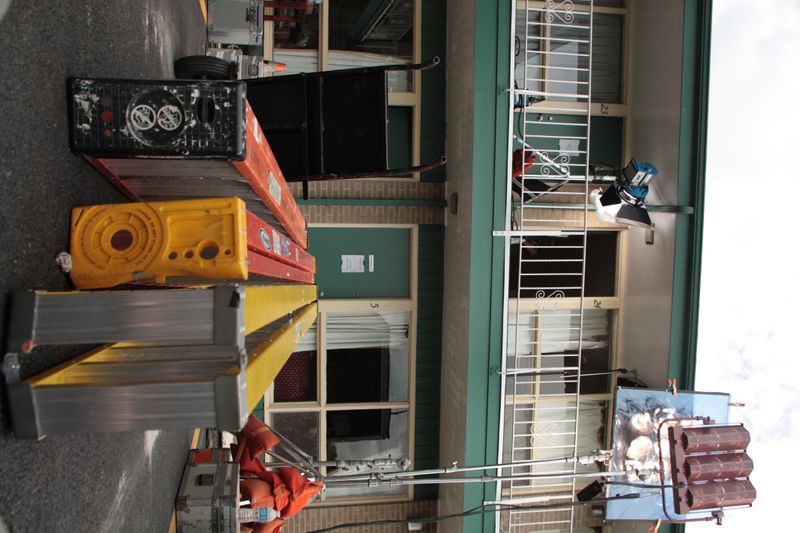 Ladders, c-stands, lights and other equipment staged in parking lot of film set at a two-story motel.