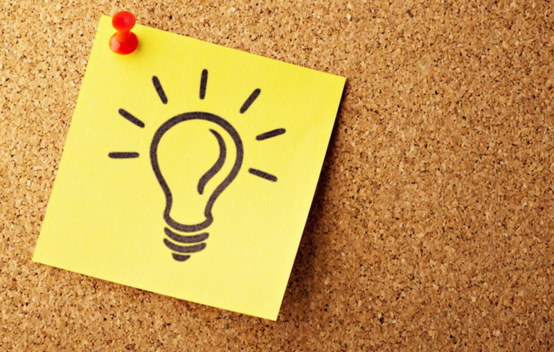 A post-it note with a lightbulb illustration pinned onto a cork board.