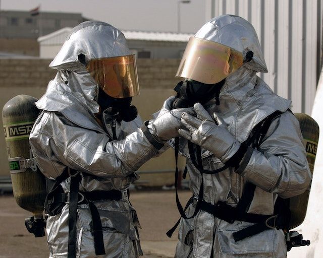 Two people wearing hazmat suits. One person is adjusting the other person's breathing apparatus.
