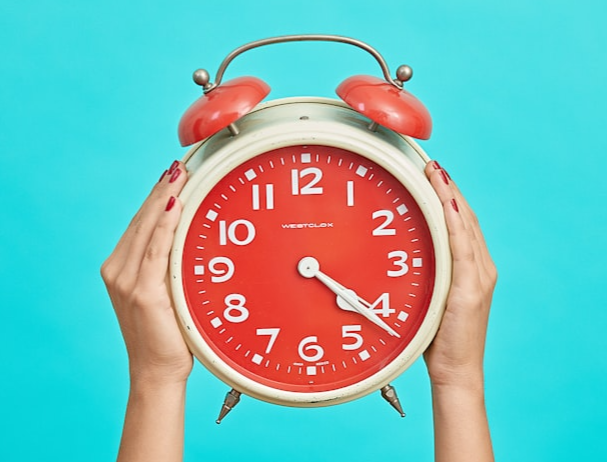 A person holding up an old-fashioned alarm clock.