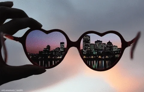 Silhouette of a hand holding heart-shaped glasses with pictures from around the world flashing through the lenses