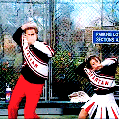 Male and female comedy actors dressed as cheerleaders perform exaggerated cheer.