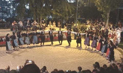 People dancing a traditional Greek dance in a public square.