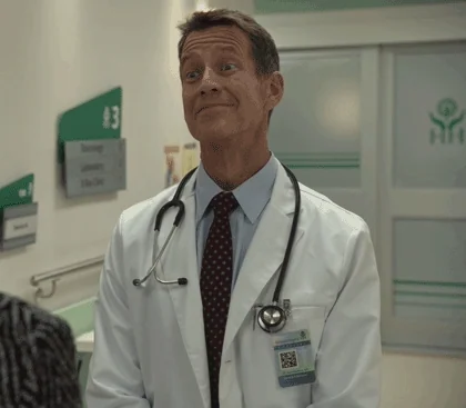 A male doctor wearing a white coat and stethoscope nods and raises his eyebrows.