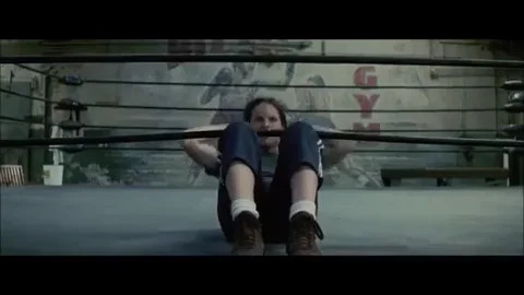 A female boxer doing sit-ups in a ring.