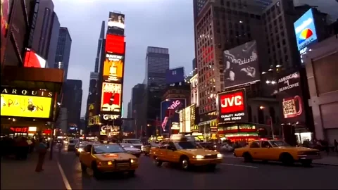 A scene of New York City, with lots of moving cars, tall buildings, and bright lights.