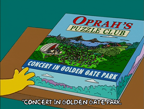 Lisa Simpson looking excitedly at a puzzle titled 'Oprah's Puzzle Club: Concert in Golden Gate Park'