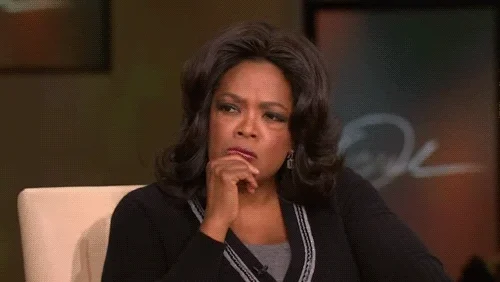 A woman (Oprah Winfrey) wearing a black sweater with her hand resting on her chin, deep in thought.