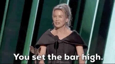 Speaking at a podium, actor Renee Zellweger lifts her hand and says 'You set the bar high.'