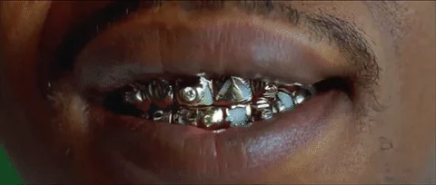 A man smiling showing gold and diamond grillz on his teeth.
