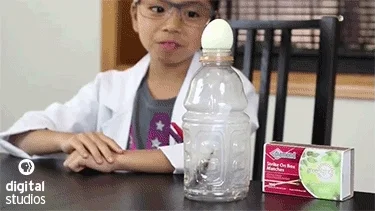 A young science student in a white coat jubilating over an egg being sucked into a bottle.