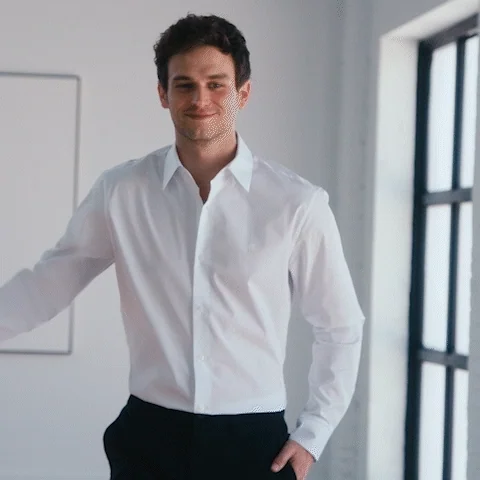 A young man in formal dress looking shy in a room.