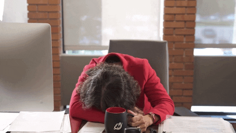 Woman takes a sip of coffee and drops head to desk as if falling asleep.