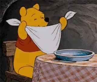 Winnie the Pooh doing a happy dance getting ready to eat at a table.