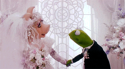 Miss piggy as a bride and kermit the frog kissing her on the cheek as the groom.