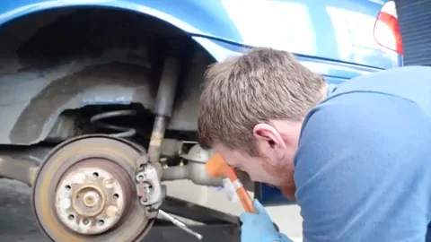 A mechanic beating on pliers with a mini orange hammer. 