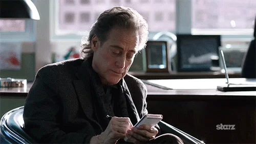 A man sitting and scribbling on a notepad while talking.