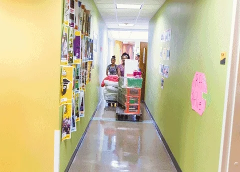 College students walking down the hallway of a residence hall with their belongings during move in day.